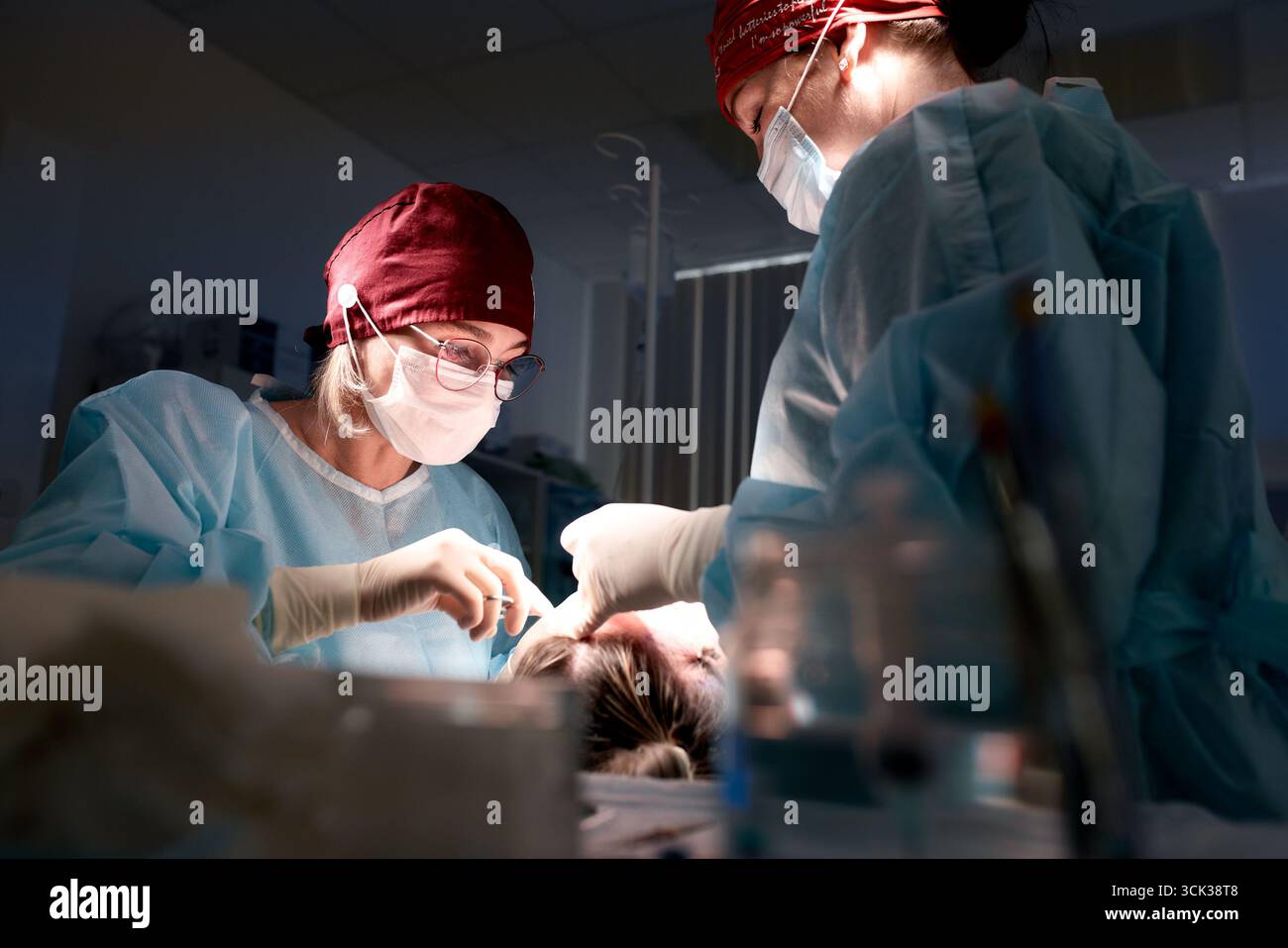 Due chirurghi vestiti con abbigliamento chirurgico sterile stanno conducendo una procedura medica in una sala operatoria ben illuminata, mostrando precisione, lavoro di squadra, e d Foto Stock