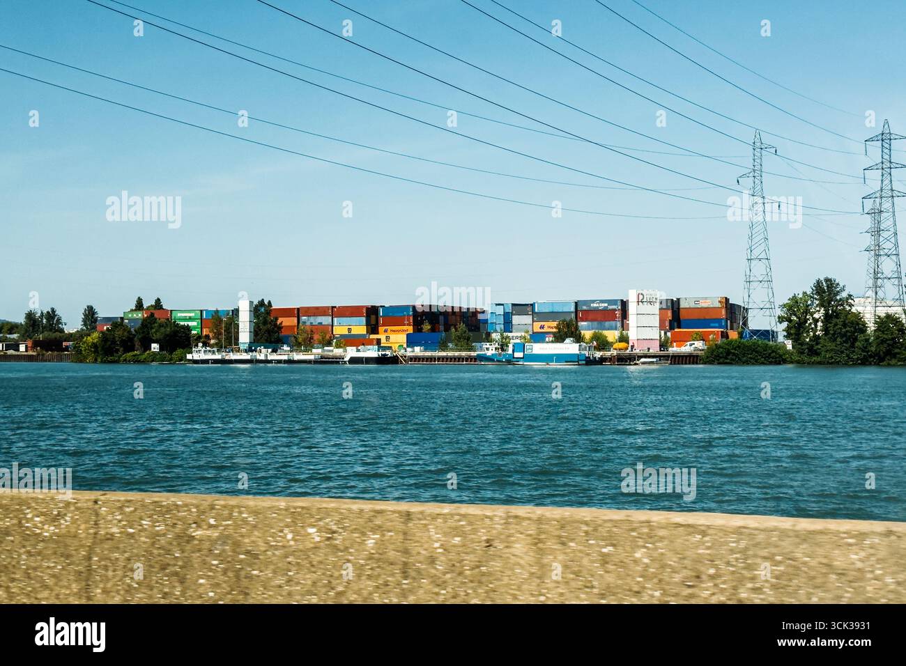 Container impilati e chiatte ancorate al Port de Lyon lungo il fiume Rodano. Lione, Francia - 19 agosto 2025 Foto Stock