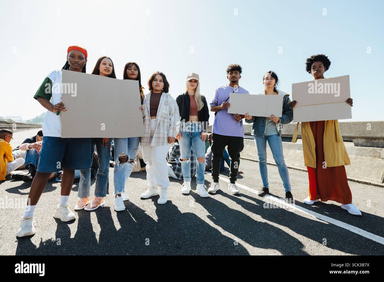 Un gruppo variegato di giovani adulti in piedi insieme su una strada urbana, tenendo dei cartelli bianchi durante una dimostrazione. Unità, attivismo, consapevolezza sociale e Foto Stock