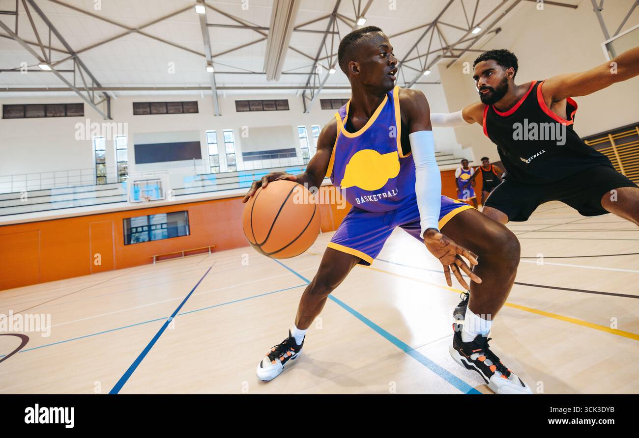 Due giocatori di basket sono impegnati in una corsa competitiva verso il cerchio su un campo al coperto illuminato, mostrando atletismo, strategia e scoraggiamento Foto Stock