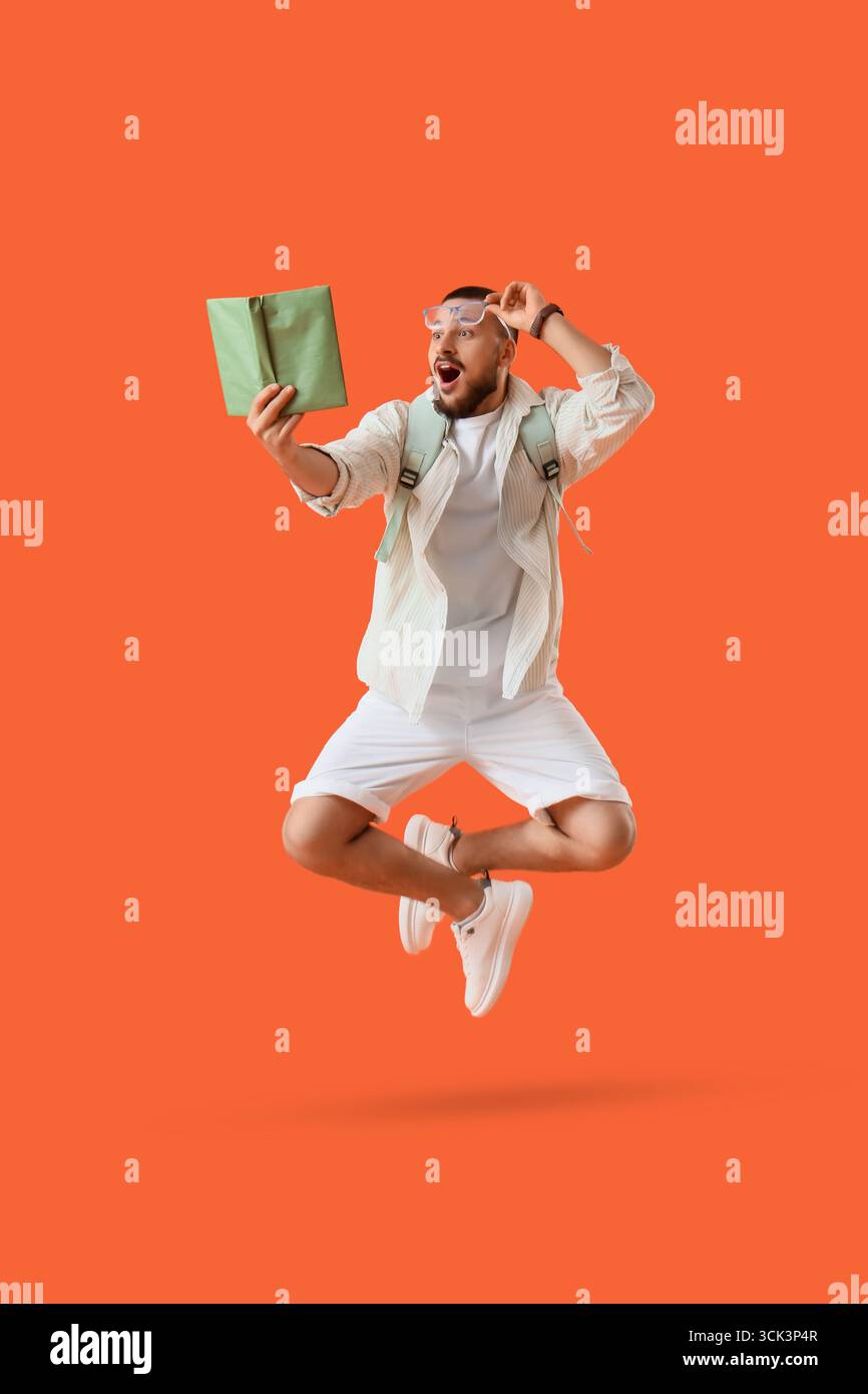Ha sorpreso il giovane con un libro che salta su sfondo arancione Foto Stock