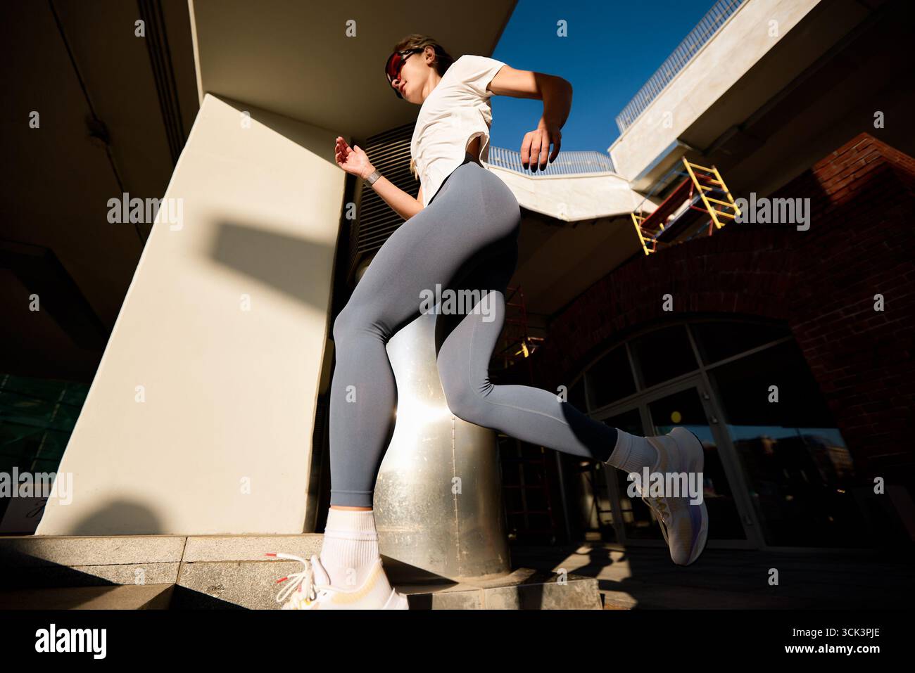 Una composizione dinamica che mostra una donna che corre all'aperto in un ambiente urbano. La sua postura atletica, unita alla luce del giorno, mette in risalto i temi Foto Stock
