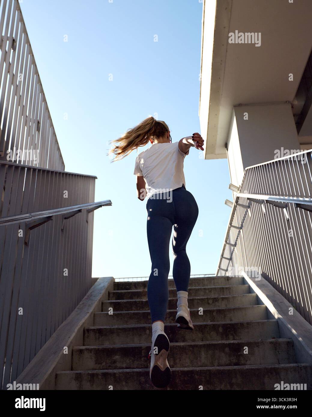 Una giovane donna che indossa un abbigliamento atletico corre su una scala all'aperto alla luce del sole. L'immagine cattura il movimento e il dinamismo dell'attività, s Foto Stock