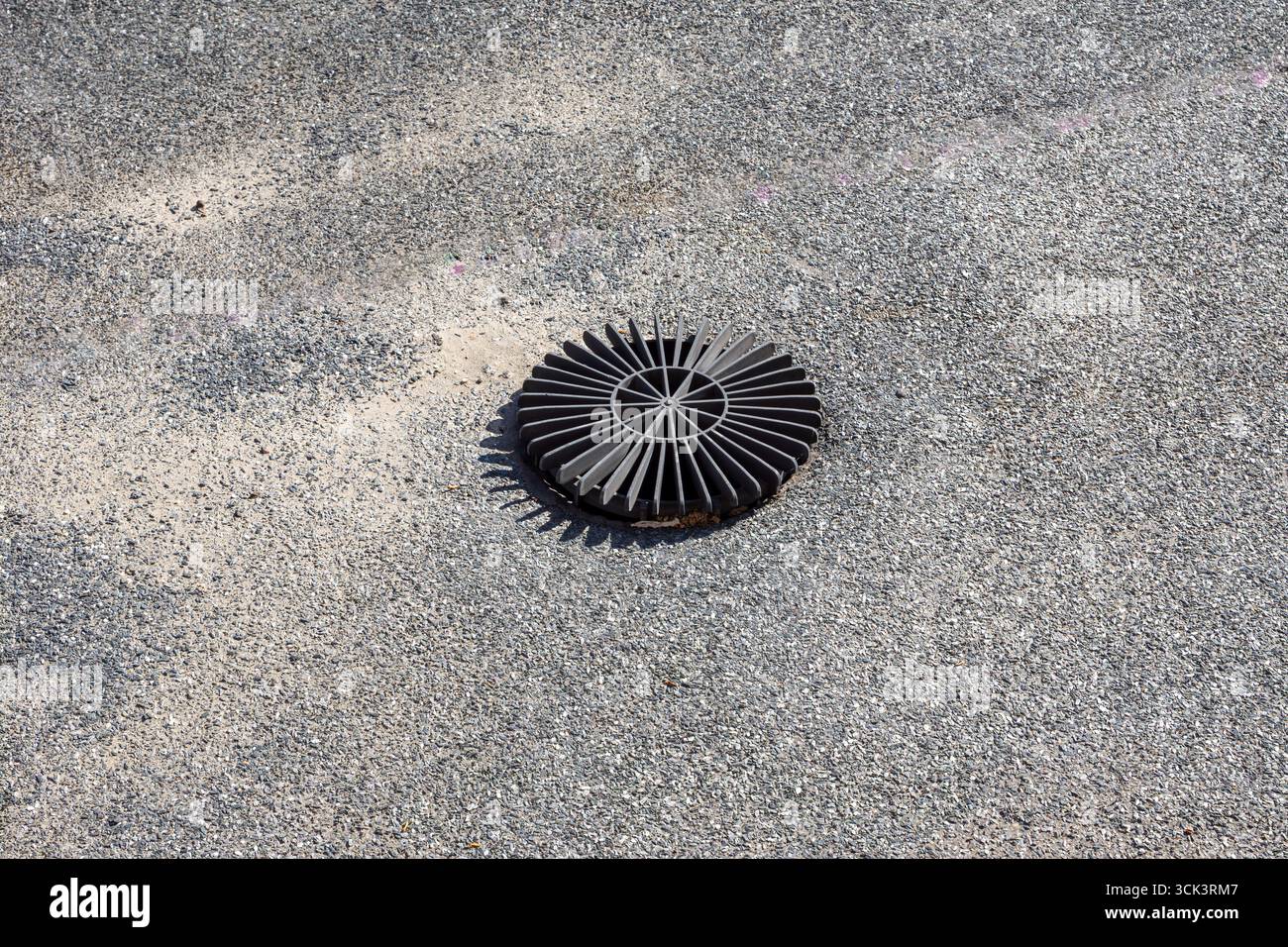 Primo piano di una griglia circolare di drenaggio dell'acqua piovana con alette radiali incorporate in un tetto piatto ricoperto da membrana bituminosa e ghiaia, che mostra il drenaggio Foto Stock