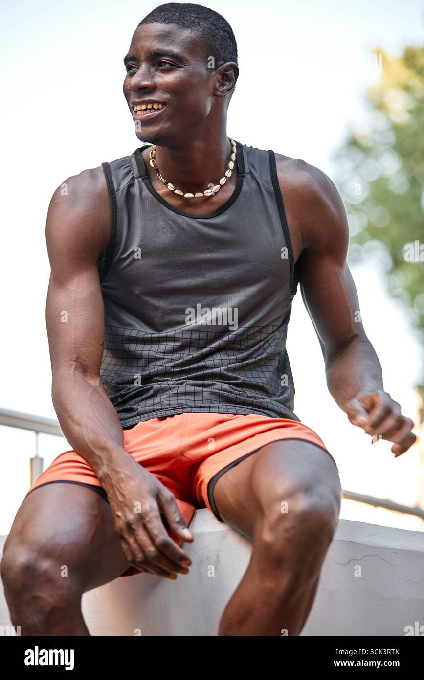 Un uomo sicuro di sé siede all'aperto indossando abiti sportivi, trasudando felicità ed energia. La posizione rilassata e allegra suggerisce uno stile di vita attivo a. Foto Stock