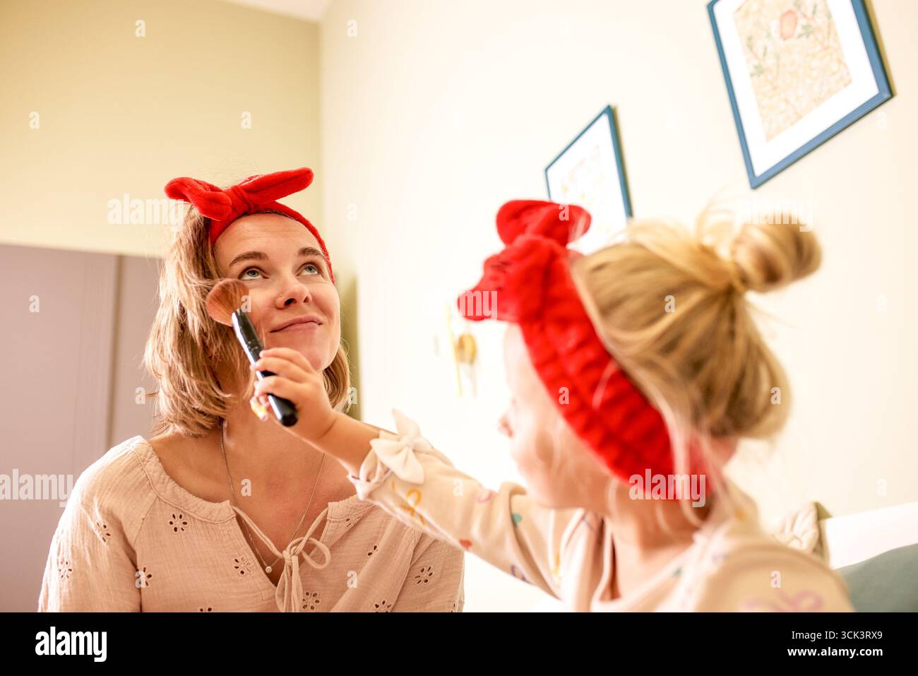 Una scena allegra di una bambina che applica il trucco sul viso di sua madre. Entrambi indossano fasce abbinate, per aggiungere un tocco di divertimento e di aderenza Foto Stock