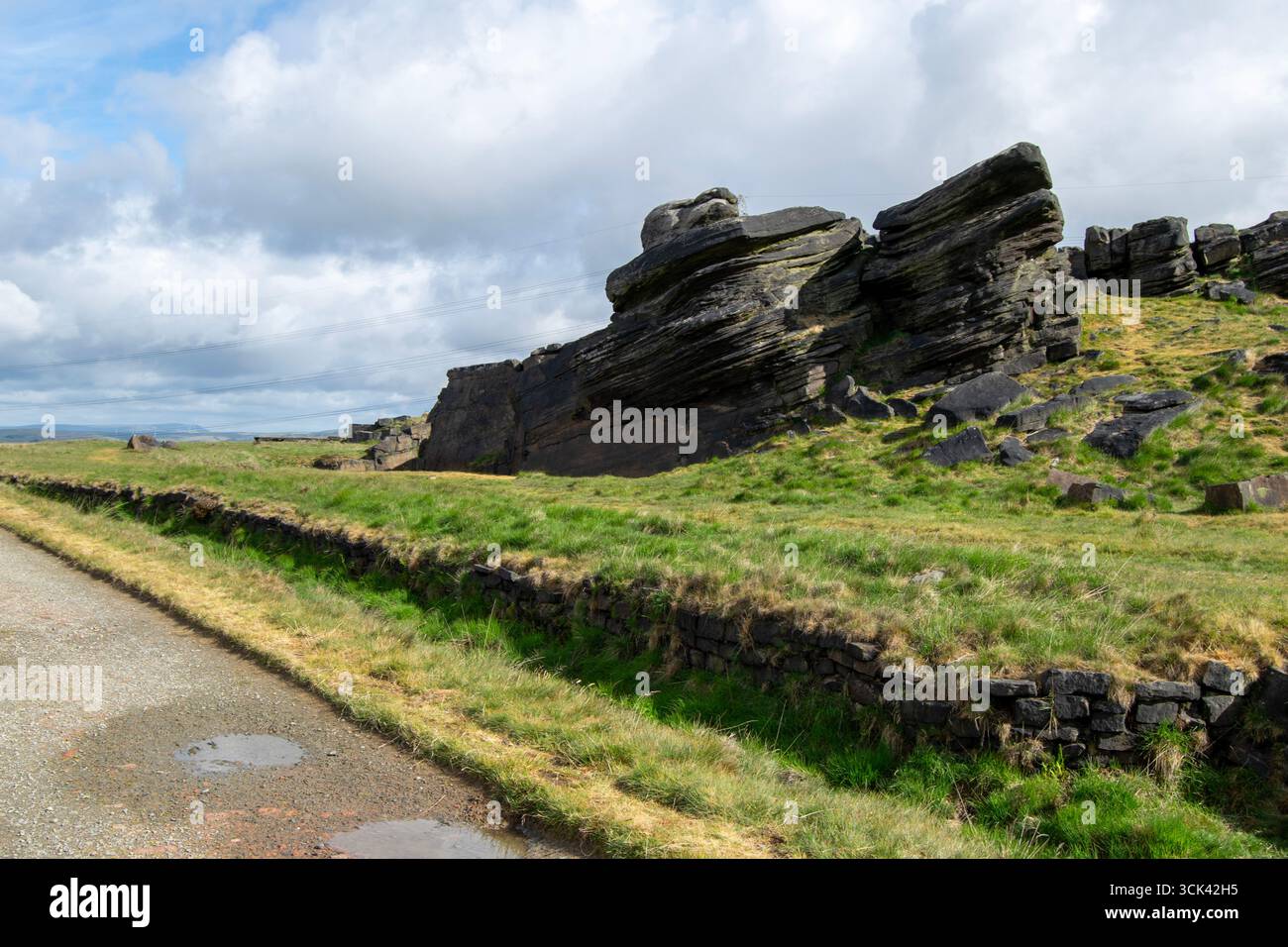 La Weathered Rain Stone e un basso muro di pietra si trovano accanto a un sentiero di brughiera sul Blackstone Edge sotto un cielo spettacolare e nuvoloso. Foto Stock