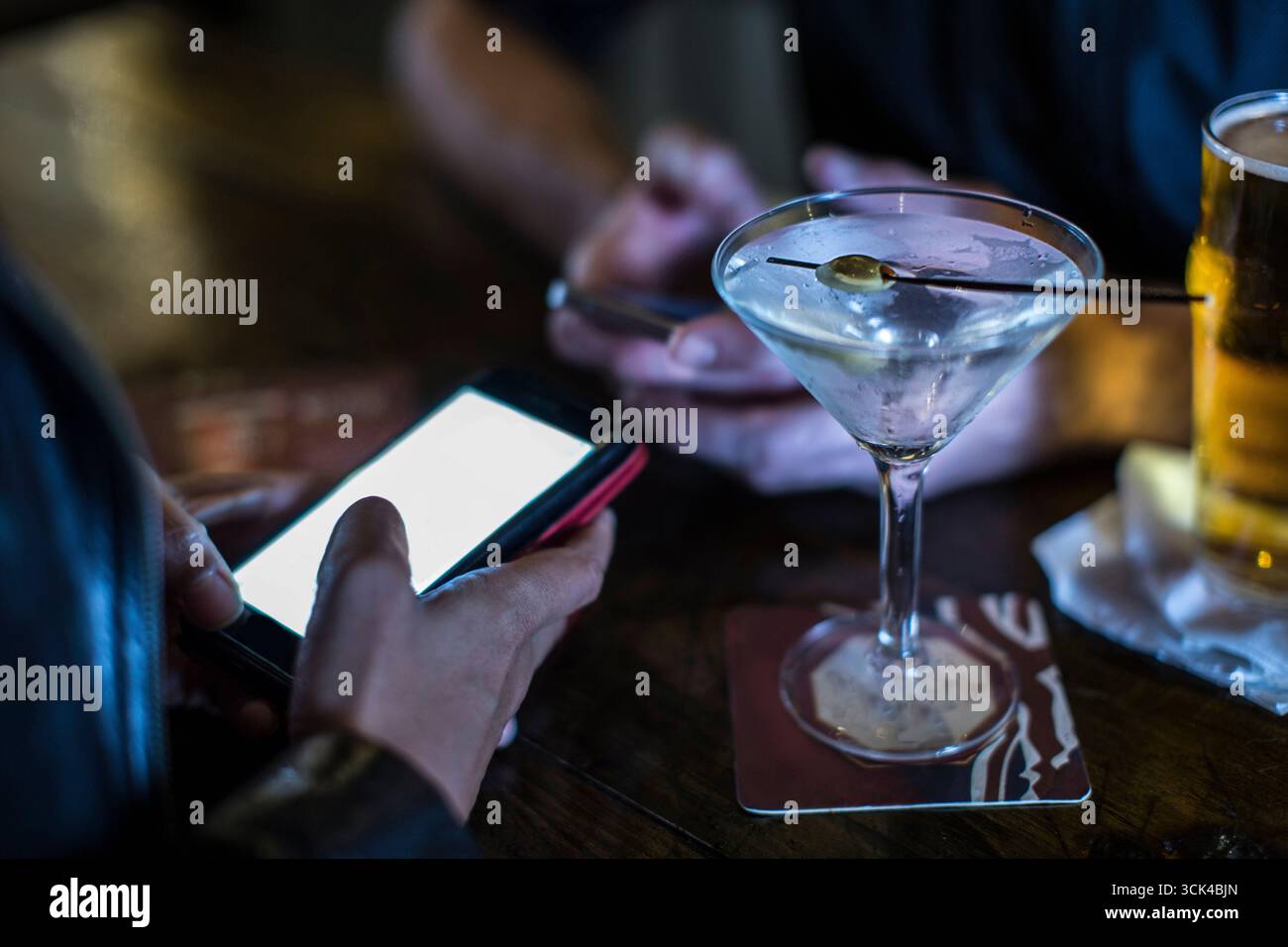 Una donna con un martini guarda il suo smartphone Foto Stock