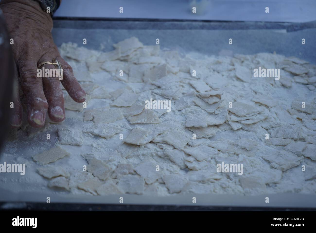 Mano di una donna anziana, con un dito di martello e un anello, che prepara la tradizionale pasta cretese mangiri su una superficie infarinata, un eccellente sfondo. Foto Stock