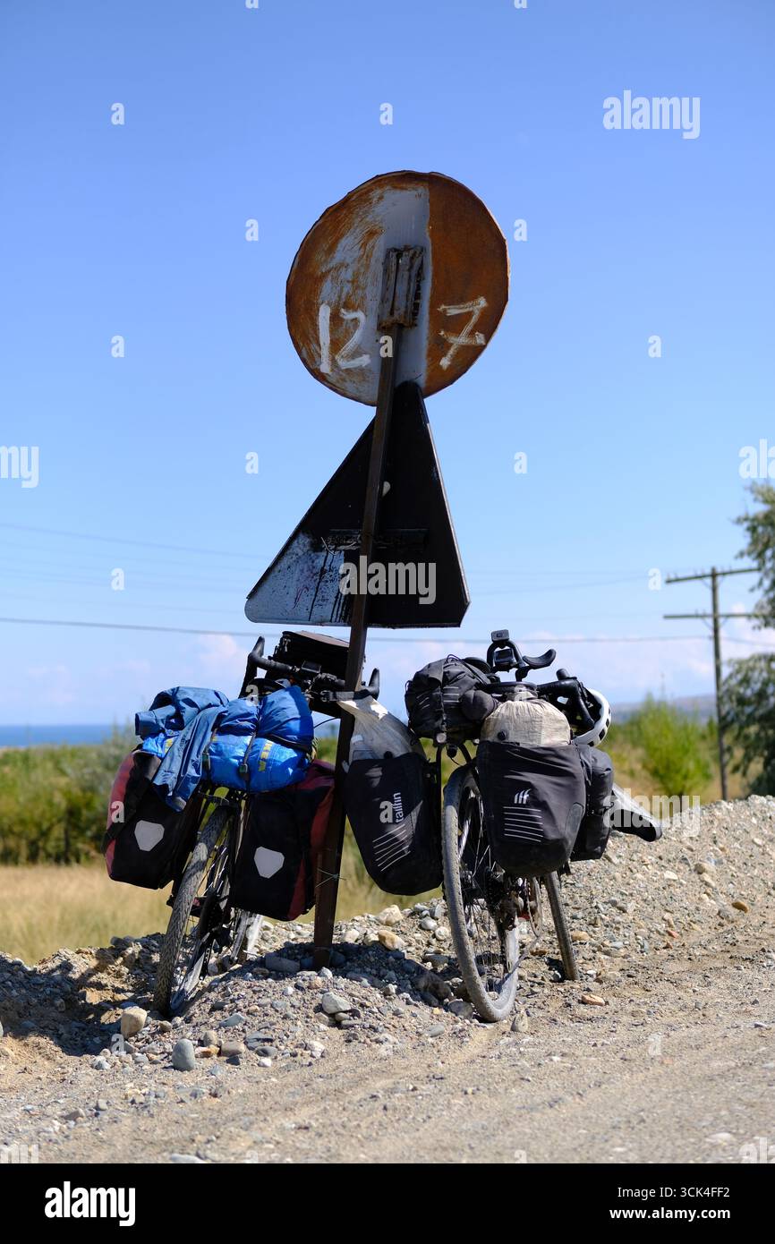 Due biciclette pesantemente caricate si appoggiano contro un cartello stradale su una strada sterrata in Kirghizistan. Foto Stock