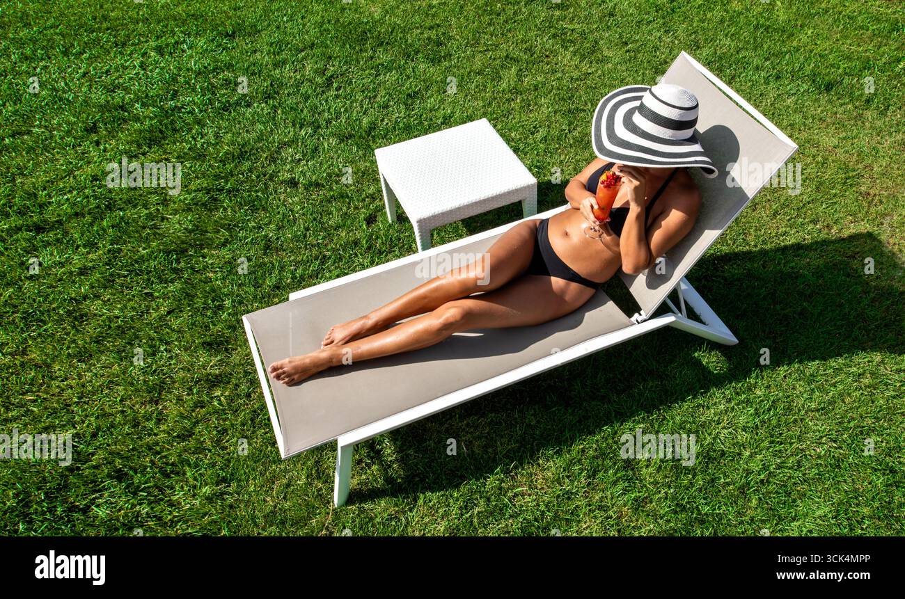 Donna in bikini che sorseggia un cocktail di frutta su una sdraio Foto Stock