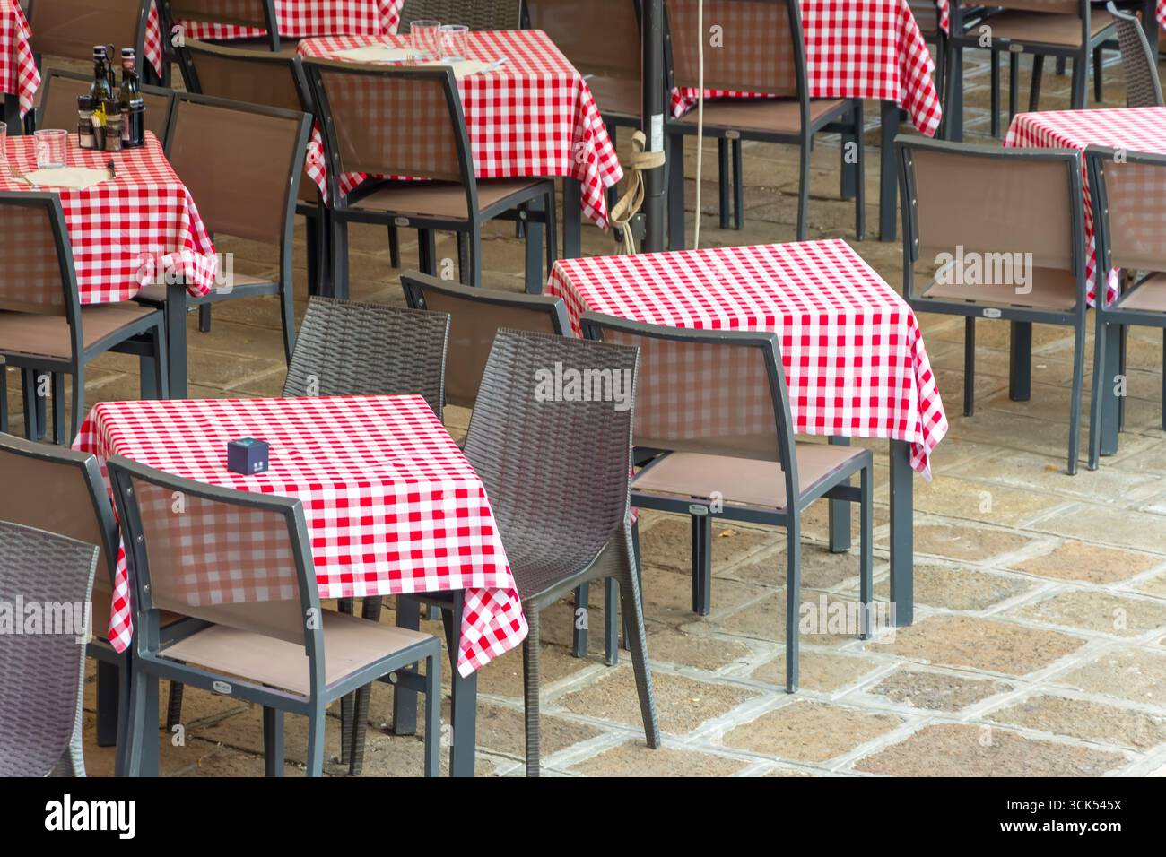 Un caffè all'aperto con tavoli vuoti coperti da tovaglie rosse e bianche Foto Stock
