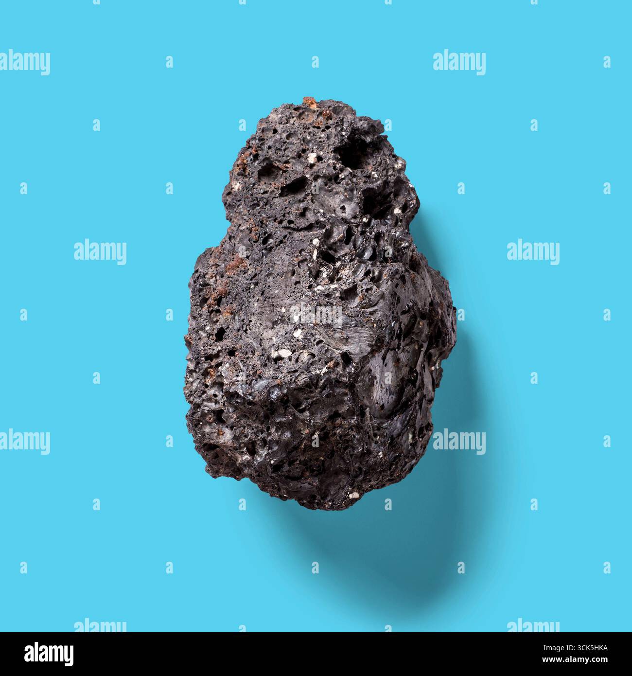 Un campione di minerale scuro e ruvido simile a una roccia vulcanica, che presenta superfici irregolari e particelle incorporate. Foto Stock