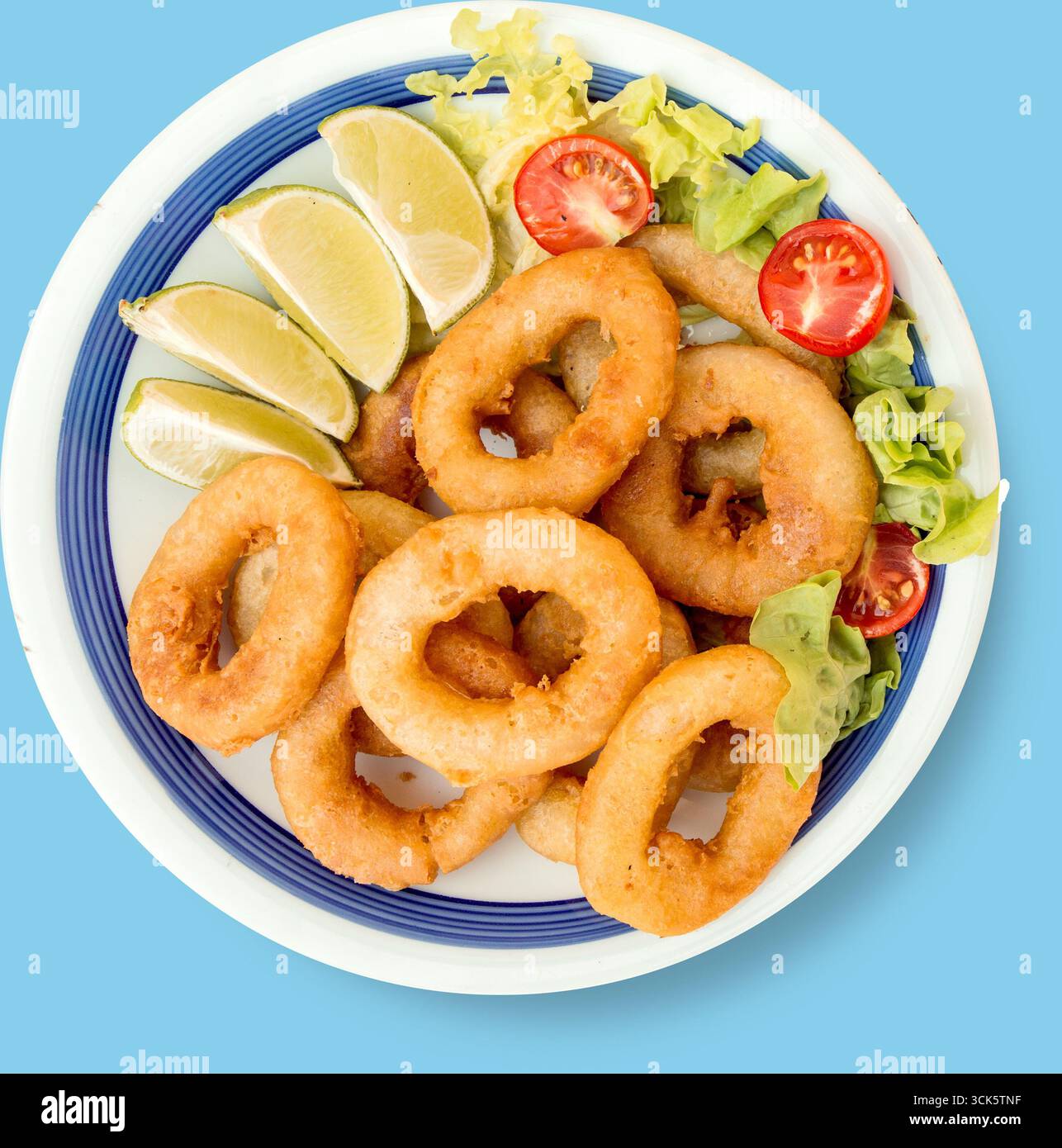 Un piatto di anelli di cipolla fritti croccanti servito con spicchi di lime e insalata fresca. Foto Stock