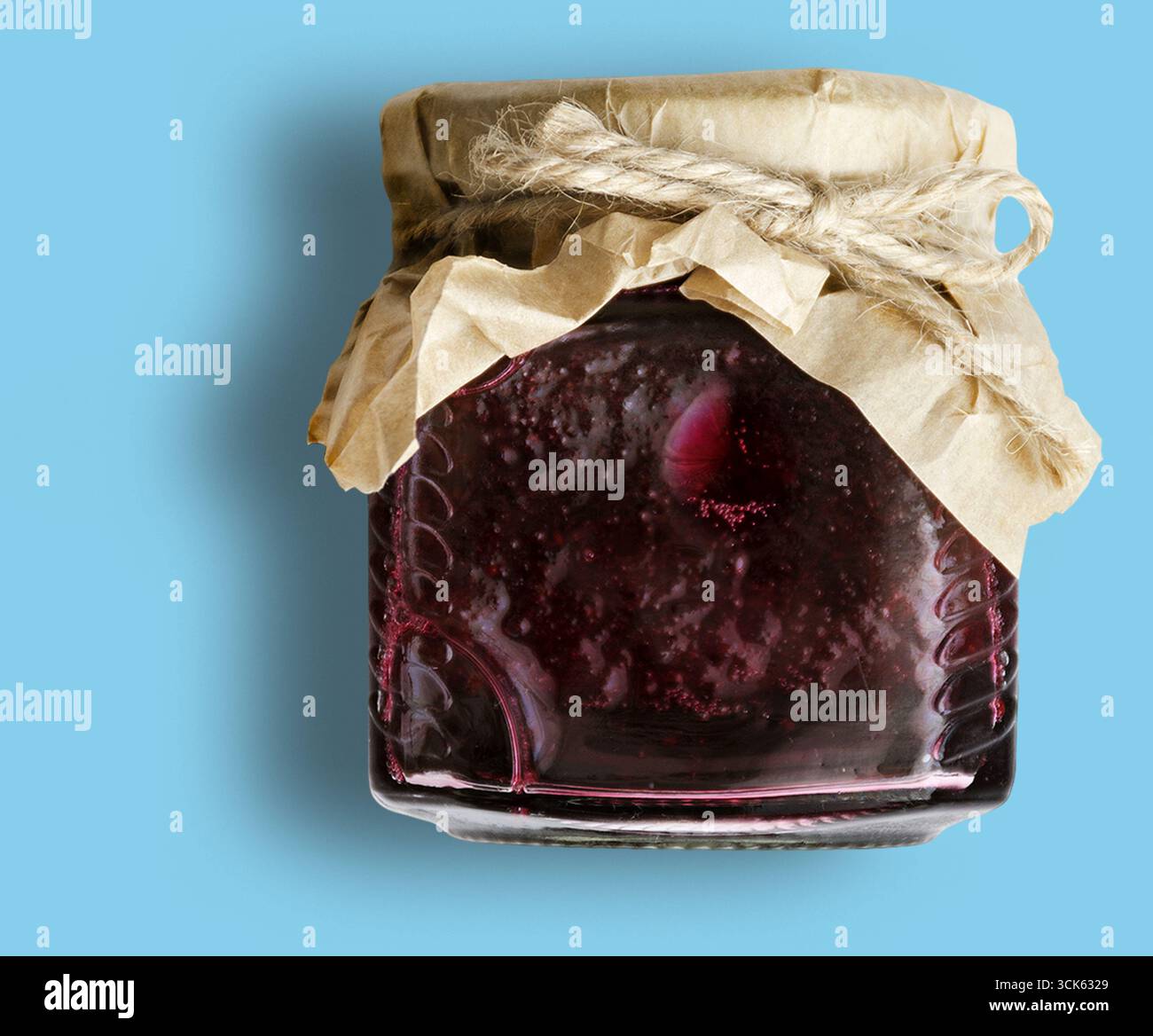 Un vasetto di marmellata di rosso scuro sigillato con un coperchio di carta e spago, che suggerisce una preparazione fatta in casa o artigianale. Foto Stock