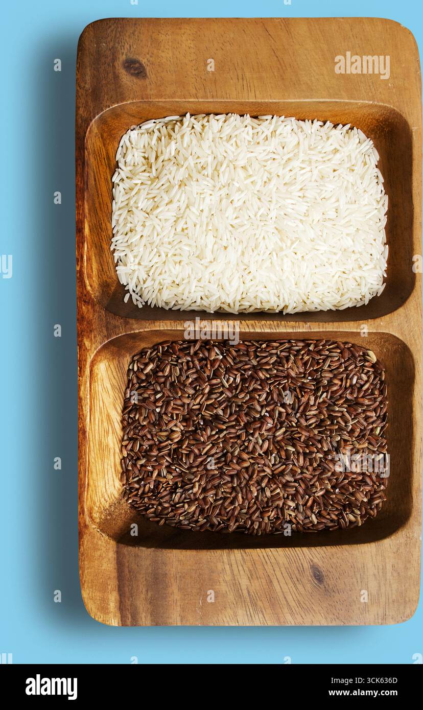 Un vassoio di legno contenente due tipi di riso bianco sulla sommità e riso integrale sotto, che mostra i loro colori e le loro consistenze distintive. Foto Stock