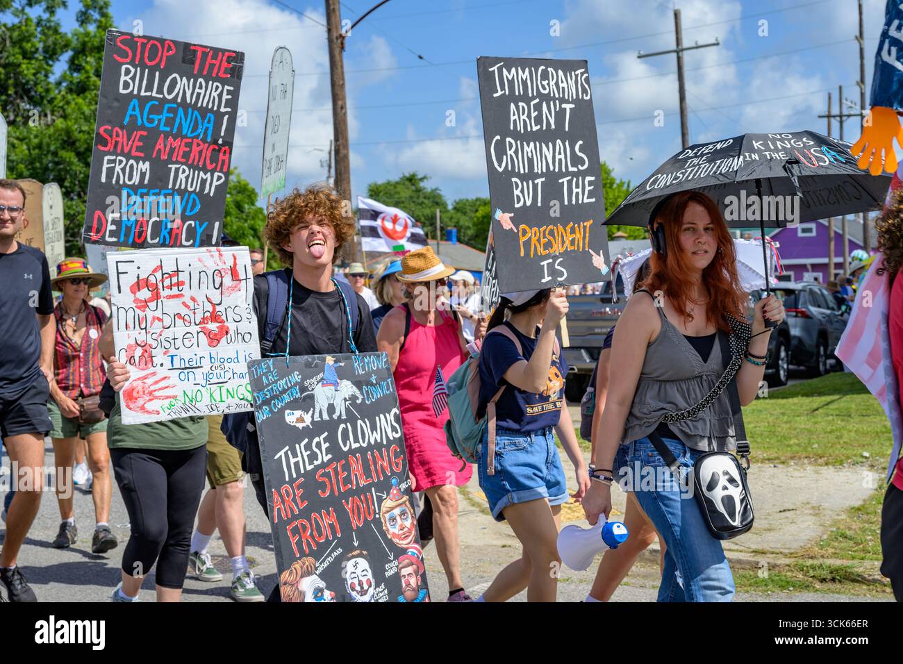 New Orleans, LOUISIANA, Stati Uniti d'America - 14 giugno 2025: Manifestanti No Kings Day generazionalmente diversi con cartelli e ombrelli, e un dimostratore anti Trump che si alza la lingua Foto Stock