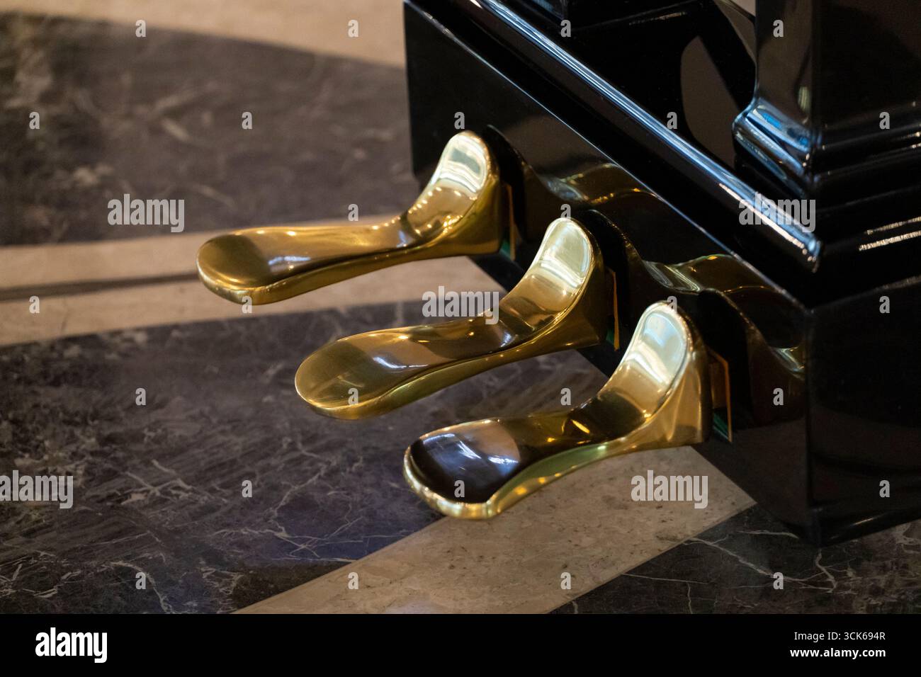 Primo piano di tre pedali in ottone lucido di un pianoforte a coda su una base nera lucida, poggiati su un pavimento in marmo fantasia. Ideale per musica, performance, e. Foto Stock