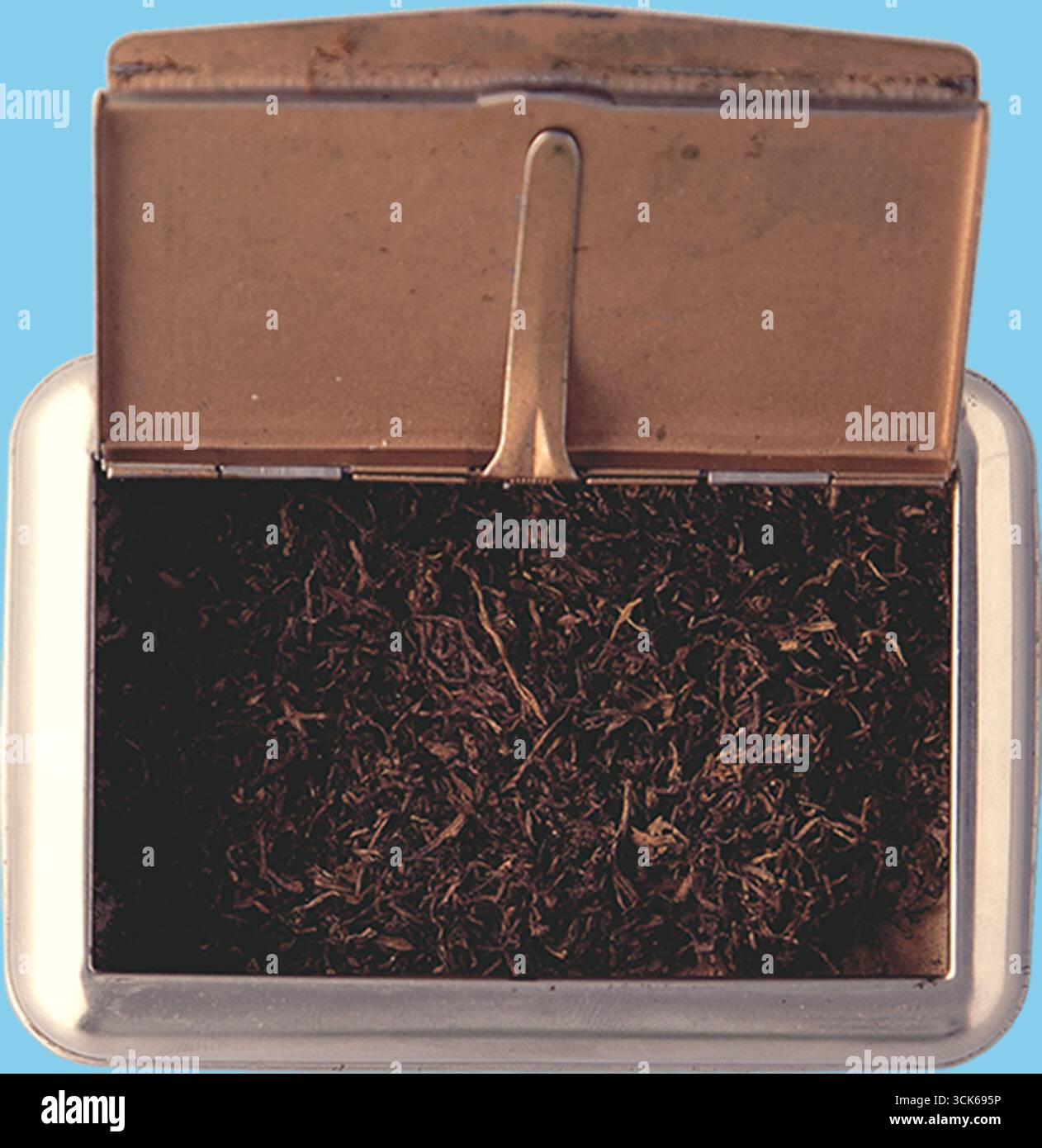 Un contenitore metallico con coperchio, riempito con materiale scuro finemente tritato, eventualmente tabacco o miscela di erbe. Foto Stock