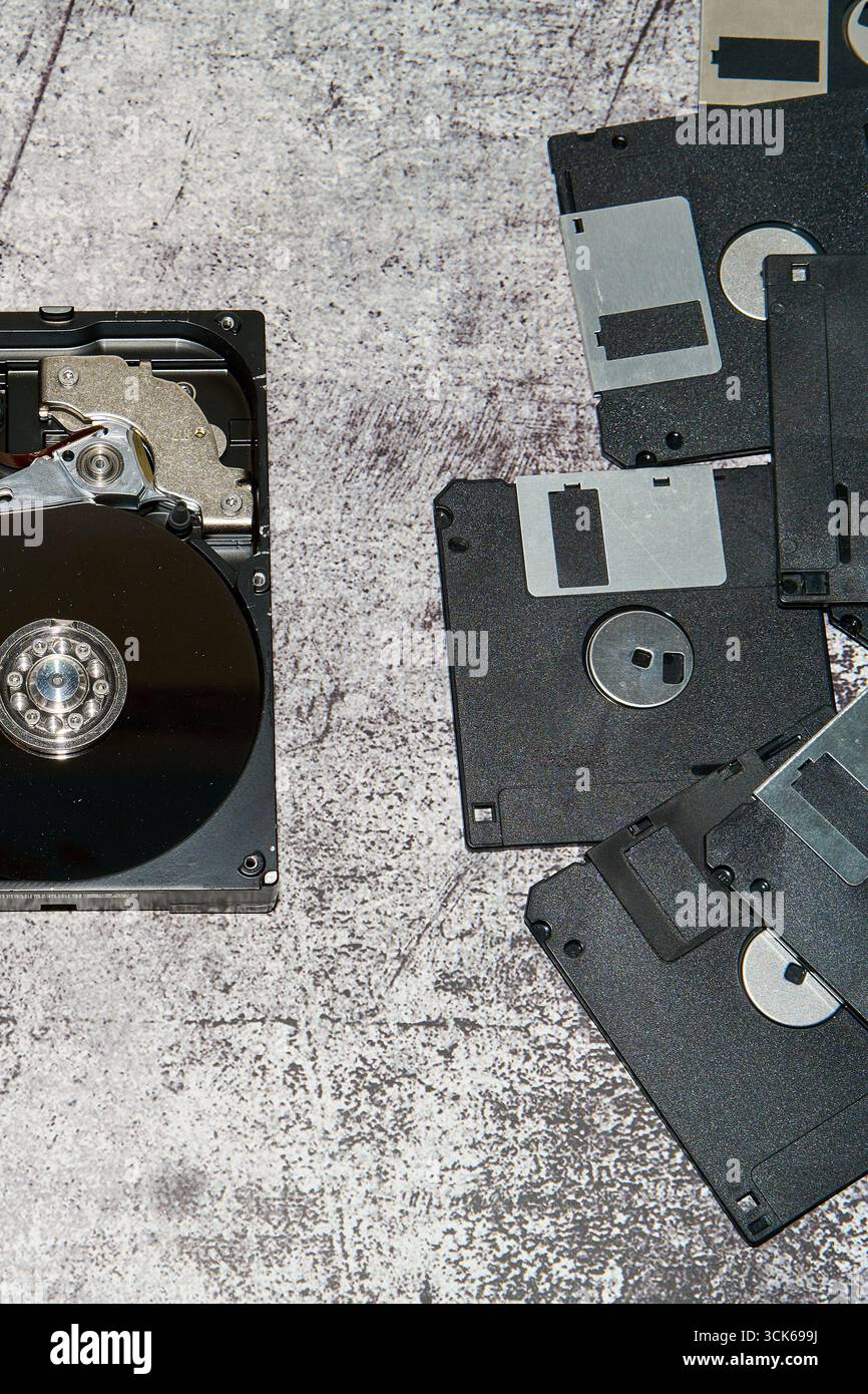 Un disco rigido aperto da 3,5 pollici accanto a diversi dischi floppy su una superficie grigia Foto Stock
