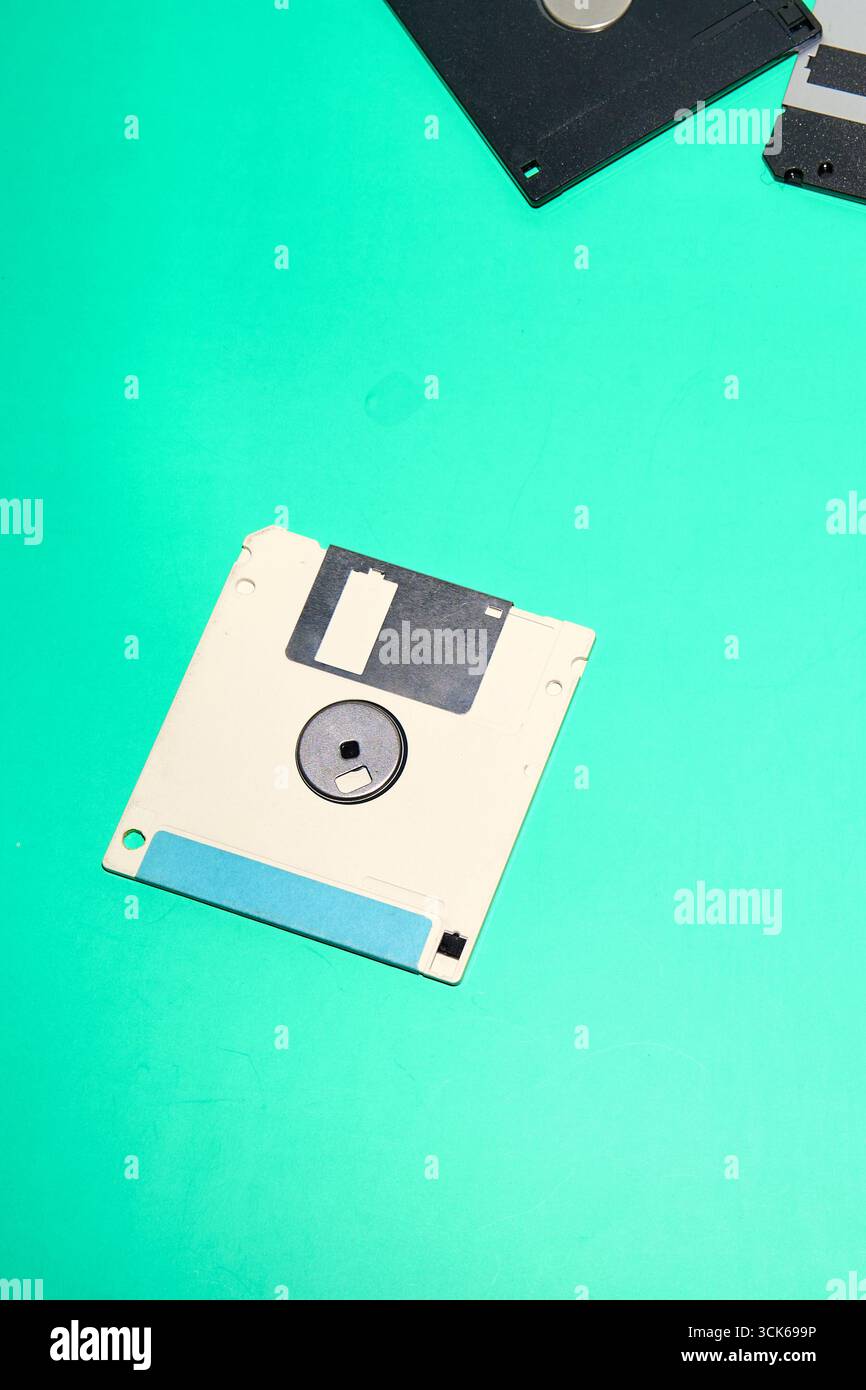Un disco floppy isolato da 3,5 pollici, con etichetta blu, è posizionato su una superficie liscia turchese Foto Stock