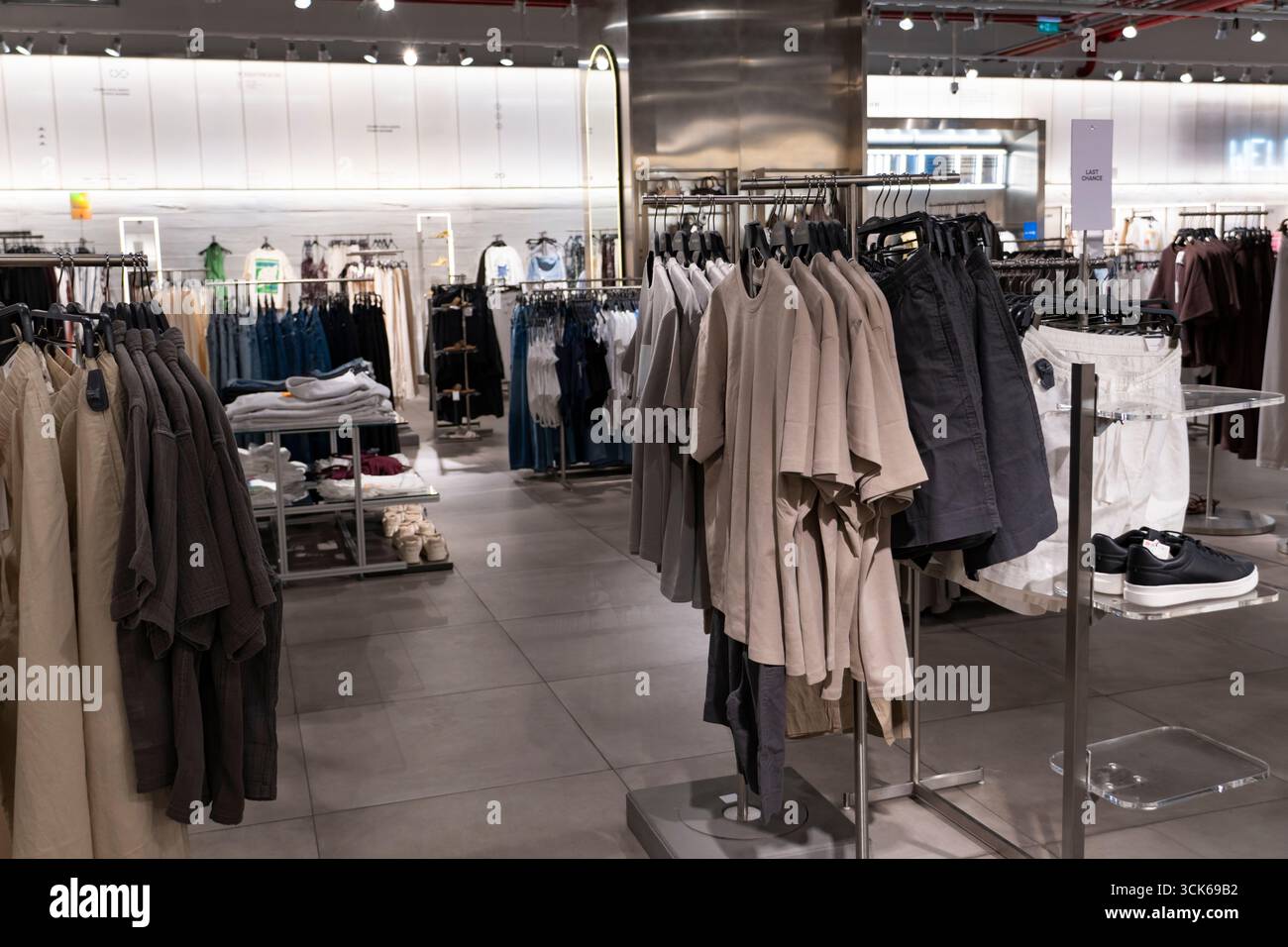 Negozio di moda luminoso e organizzato con abbigliamento, sneaker dalle tonalità neutre e layout minimalista pulito, ideale per mostrare merchandising e shopping Foto Stock