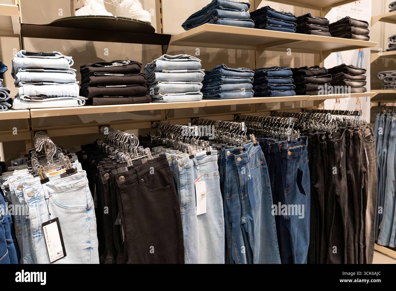 Pile di jeans blu disposte ordinatamente su scaffali di legno in un negozio di abbigliamento, che espone la moda al dettaglio e il concetto di merchandising Foto Stock