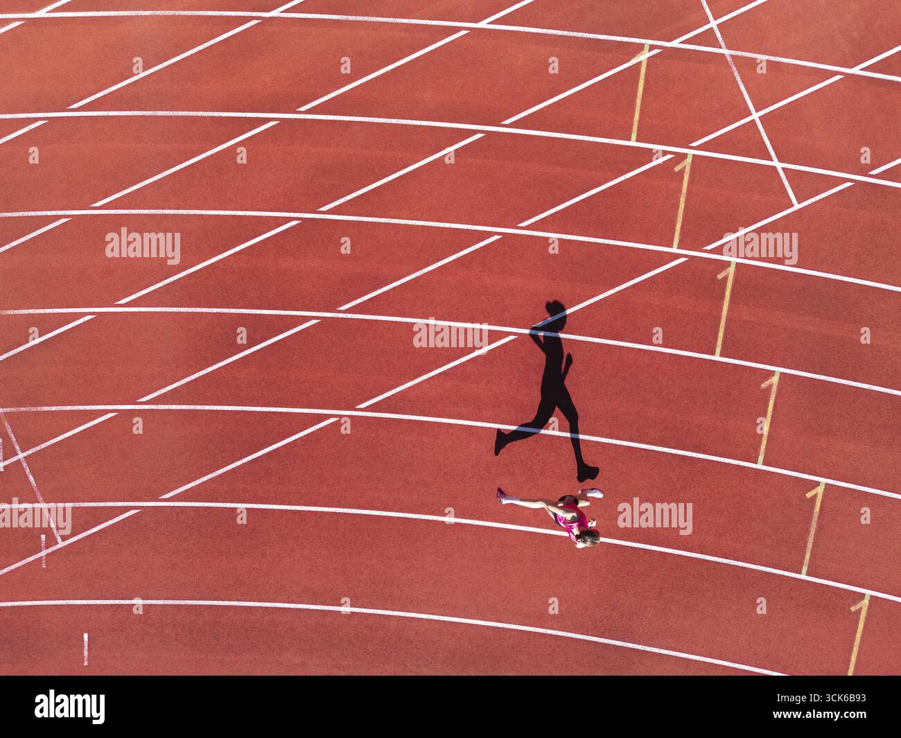 Vista aerea di una donna (runner) su una pista rossa di atletica (pista in tartan) con ombra come silhouette Foto Stock
