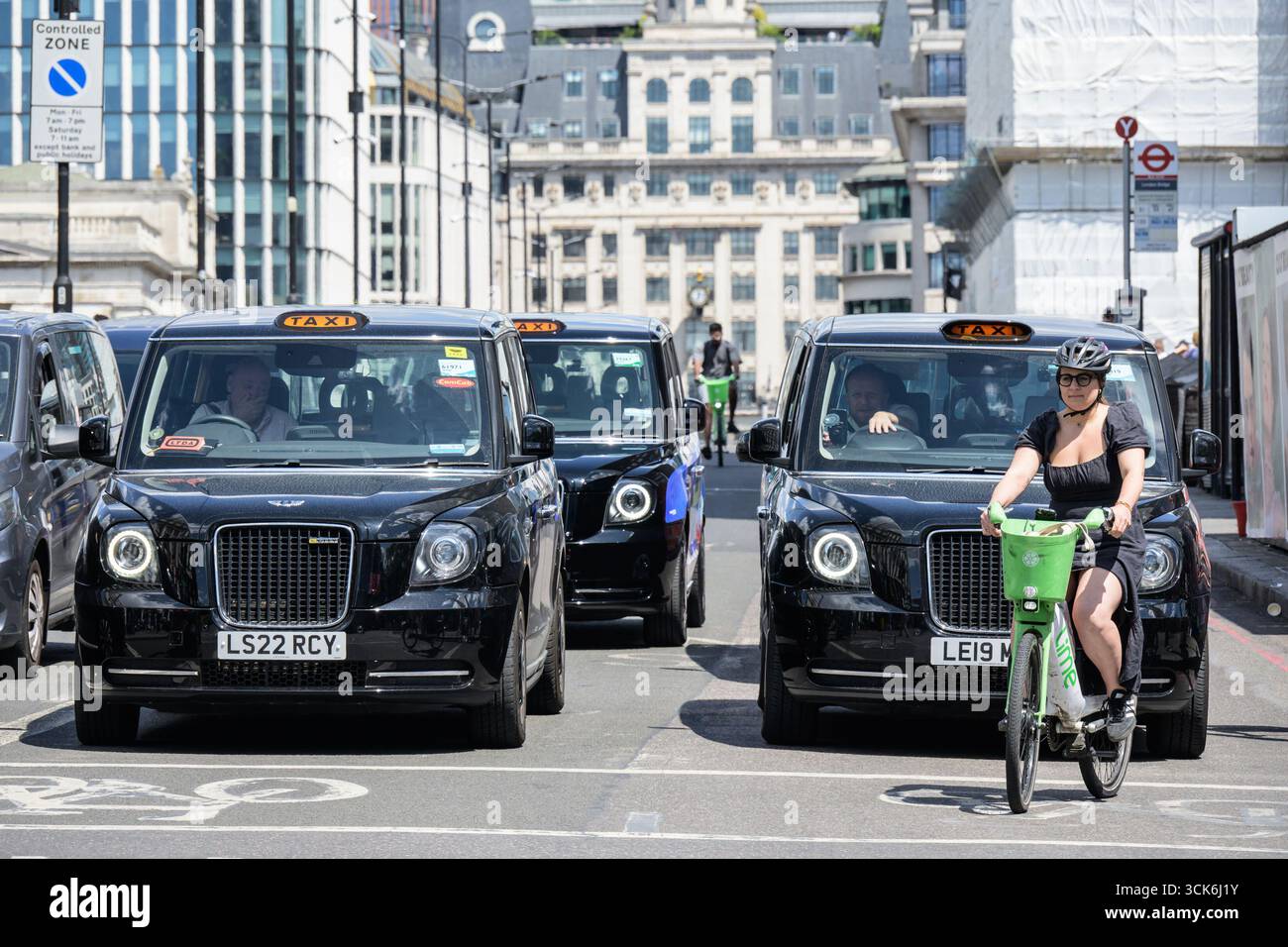 Londra, Regno Unito. Taxi neri di Londra e ciclista su una Lime noleggiata che attraversa il London Bridge, visto da sud. Foto Stock