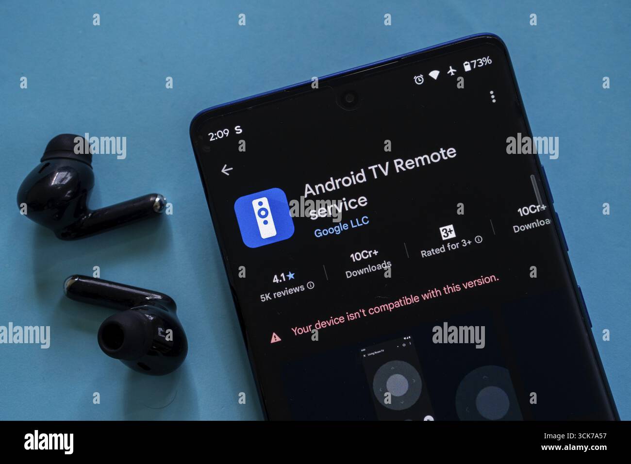 Schermo dello smartphone che visualizza l'app Android TV Remote Service, auricolari neri, sfondo blu Foto Stock