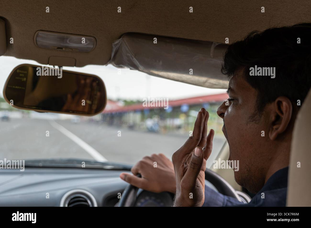 Un conducente mostra segni di stanchezza durante l'attesa in un casello, segnalando un lungo viaggio. Foto Stock