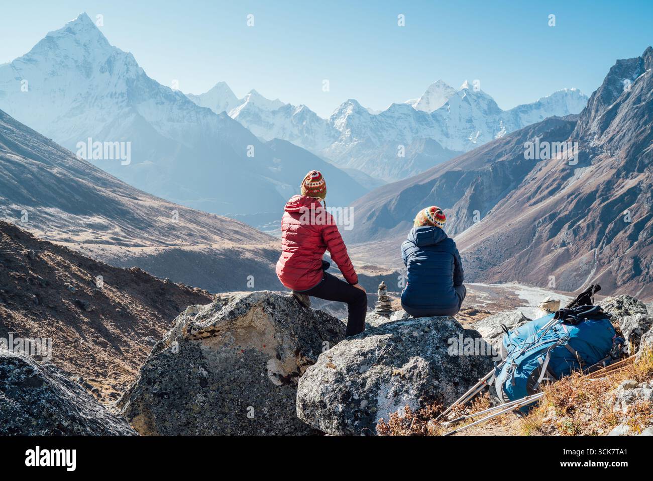 Coppia riposante sul percorso di trekking Everest base Camp vicino Dughla 4620m. Backpackers sinistra zaini e bastoni da trekking e godendo vista valle con Foto Stock