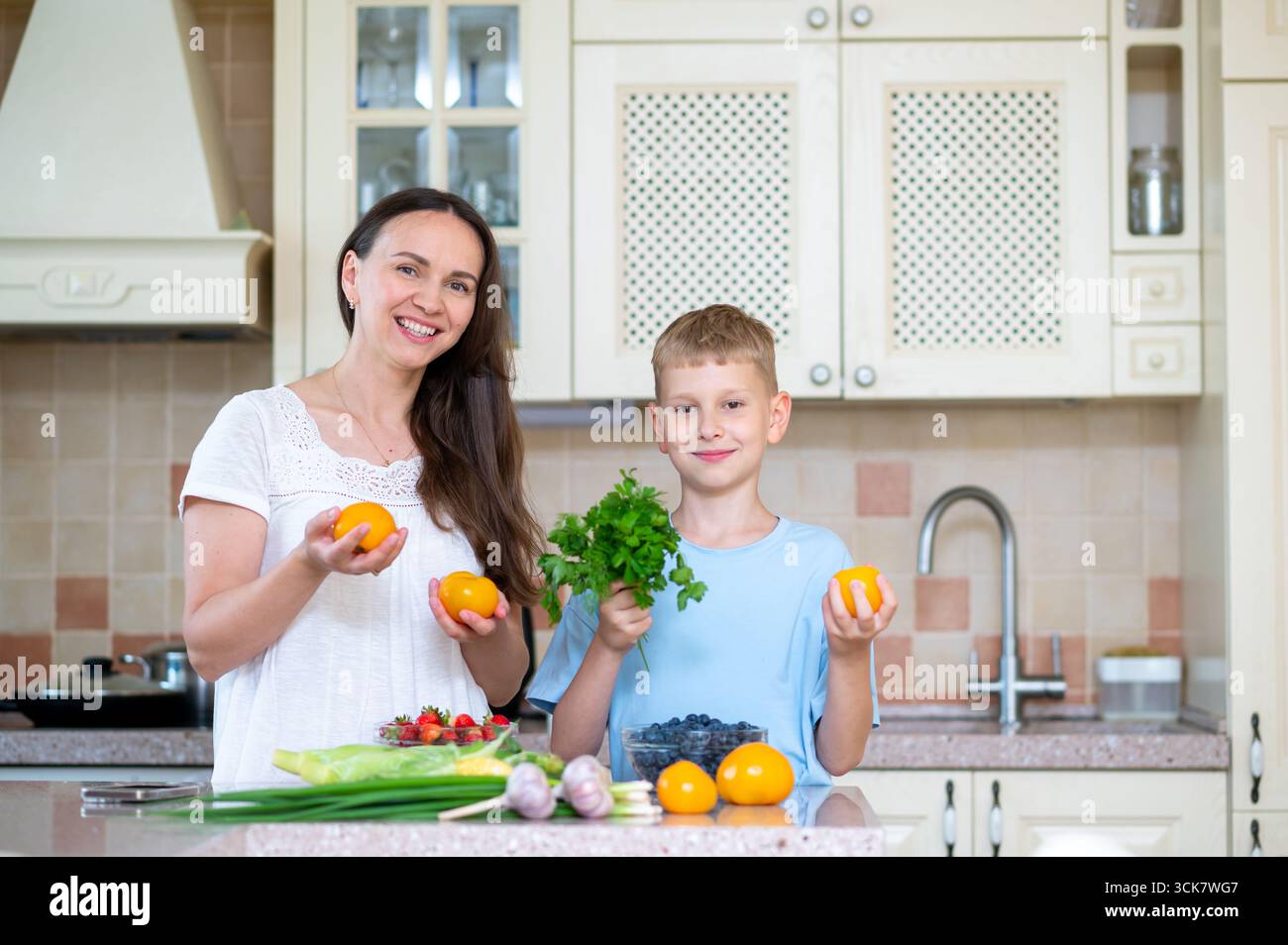 Donna e ragazzo mostrano cipolla verde e pomodori insieme. Concetto di insegnare ai bambini mangiare sano attraverso lo stile di vita familiare Foto Stock