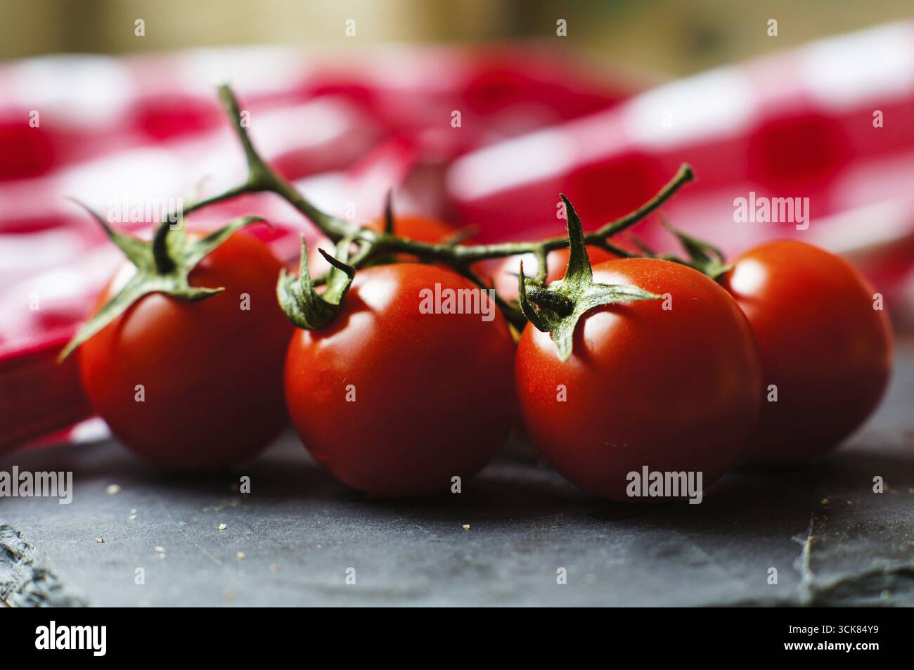 Mazzo di pomodori ciliegini rossi maturi freschi ricchi di antiossidanti e vitamine sulla vite su un bancone da cucina grigio scuro con spazio imbottito Foto Stock