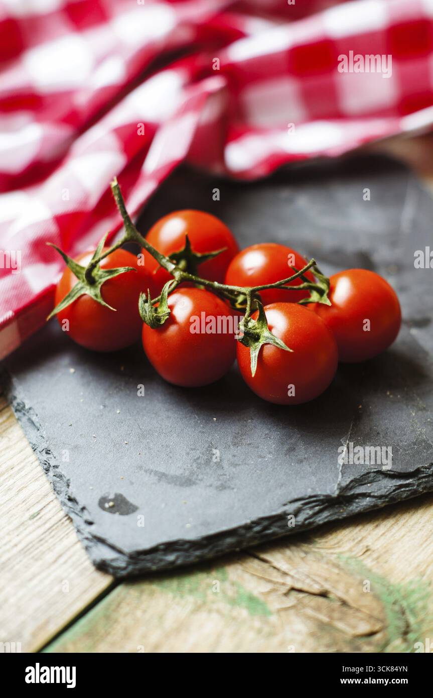 Mazzo di pomodori ciliegini rossi maturi freschi ricchi di antiossidanti e vitamine sulla vite su un bancone da cucina grigio scuro con spazio imbottito Foto Stock