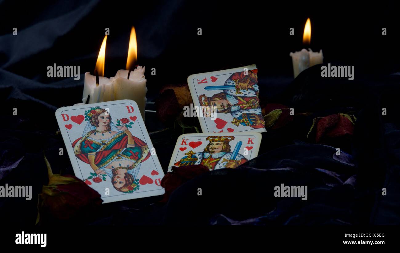 Regina dei cuori, Re dei cuori di un gioco di carte su sfondo nero. Candele accese. Concetto di separazione, nuovo amore. Foto Stock