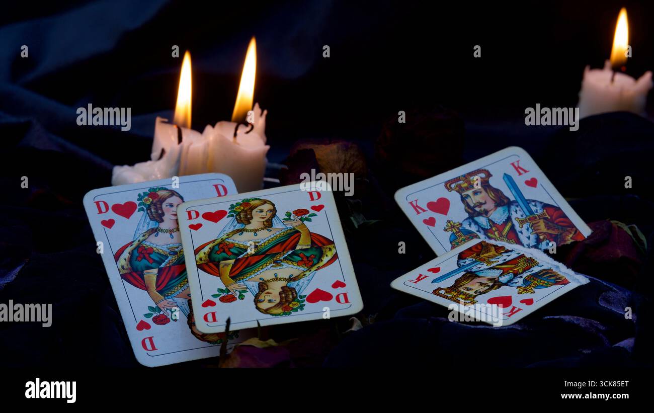 Regina dei cuori, Re dei cuori di un gioco di carte su sfondo nero. Candele accese. Concetto di separazione, nuovo amore. Foto Stock