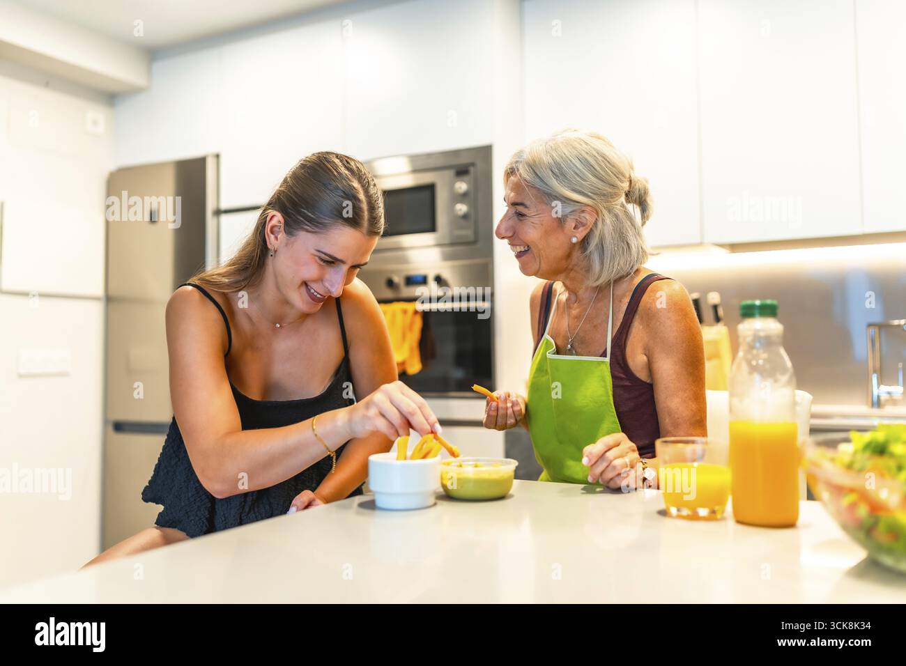 Donna anziana e giovane che condividono un momento di gioia in una cucina moderna, preparano il cibo e si legano a un pasto Foto Stock
