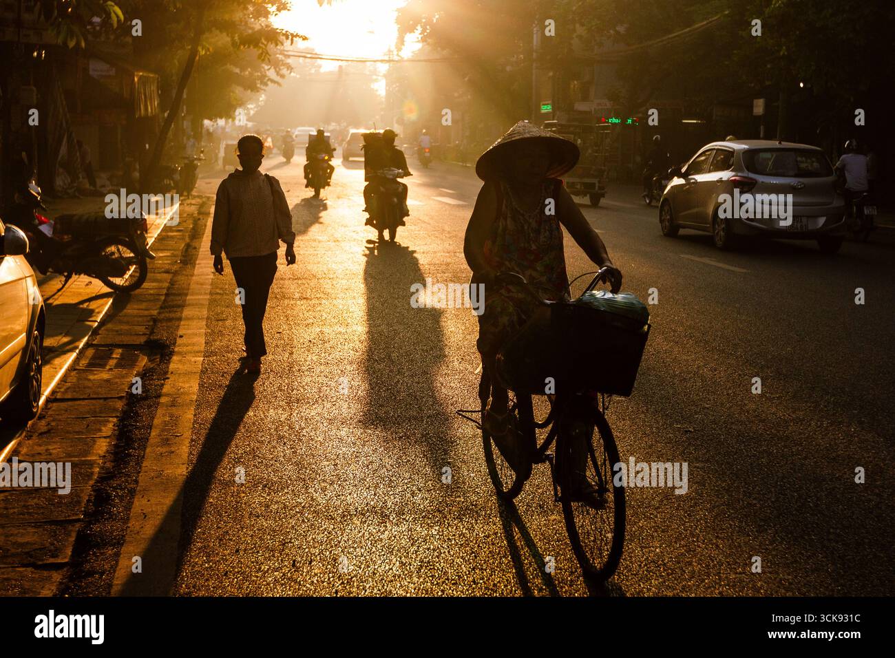 L'alba dorata illumina una strada vivace nel quartiere vecchio di Hanoi, Vietnam, con pedoni sagomati. Foto Stock