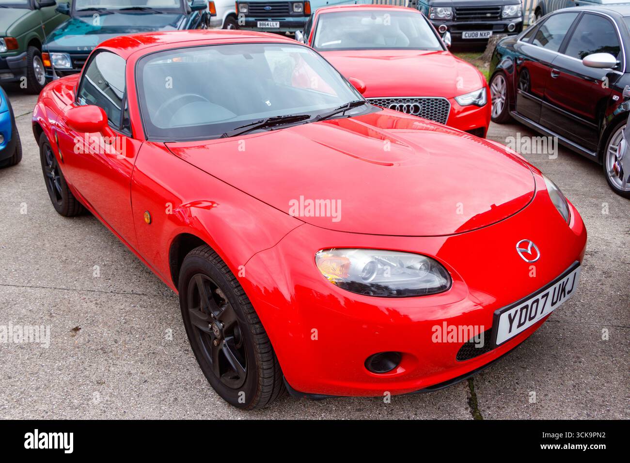 Auto sportiva rossa Mazda MX-5 parcheggiata in un sacco con vari altri veicoli sullo sfondo in una giornata di sole Foto Stock