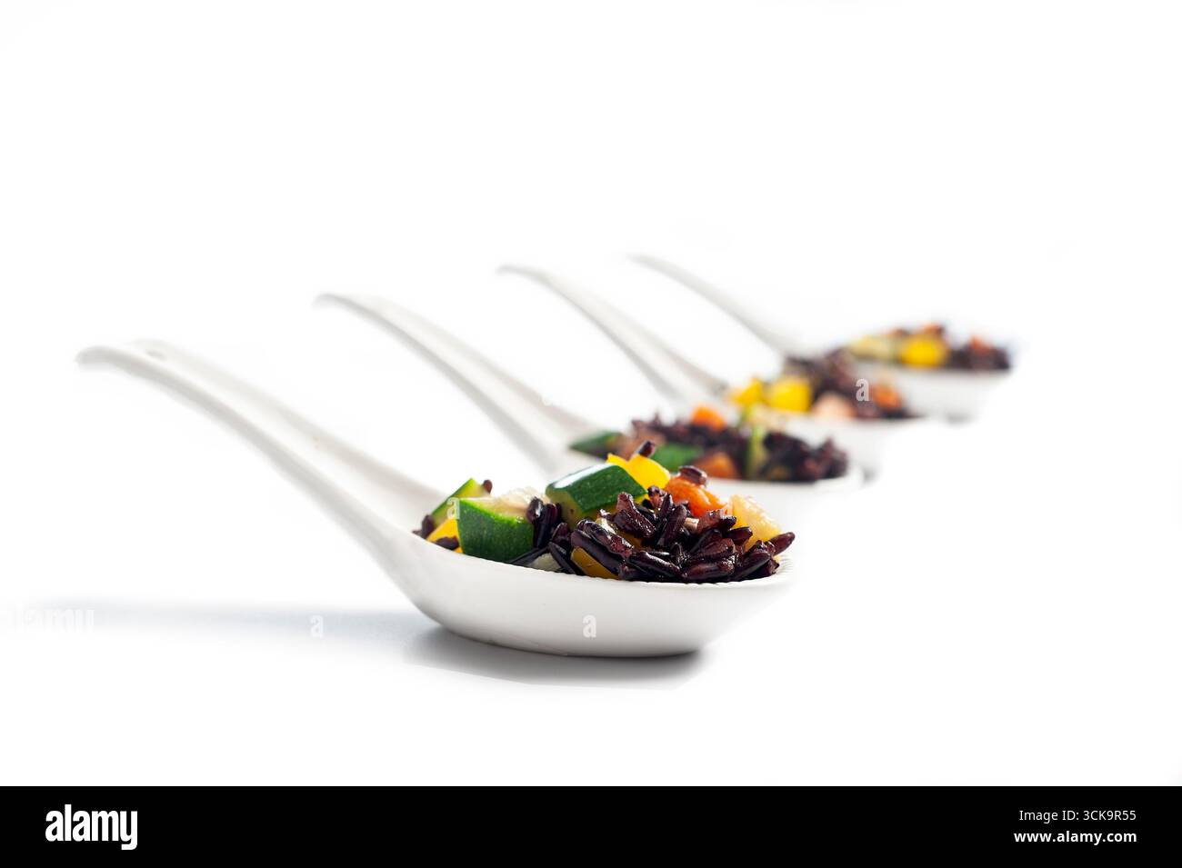 Finger food, riso Venere con verdure miste in cucchiaio, sfondo bianco Foto Stock