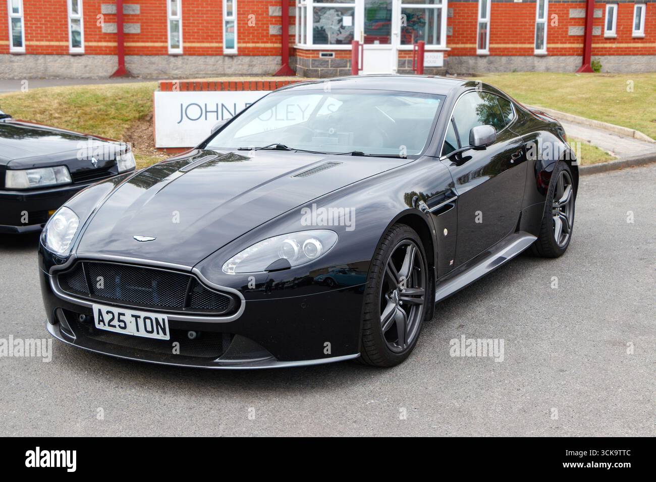 Un'elegante auto sportiva nera Aston Martin Vantage V8, parcheggiata all'aperto con moderni edifici in mattoni sullo sfondo Foto Stock
