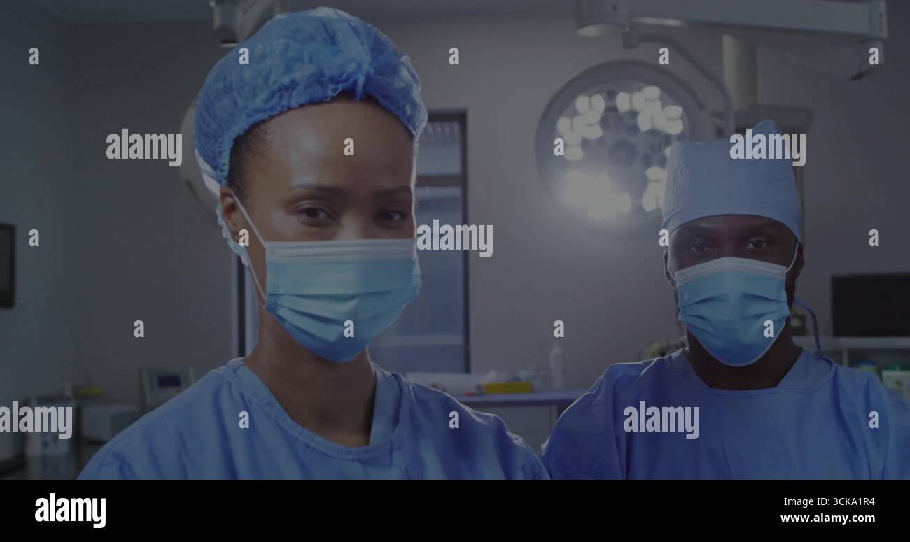 Chirurghi in piedi che indossano scrub blu e maschere in sala operatoria, lampada chirurgica, vassoio per strumenti Foto Stock
