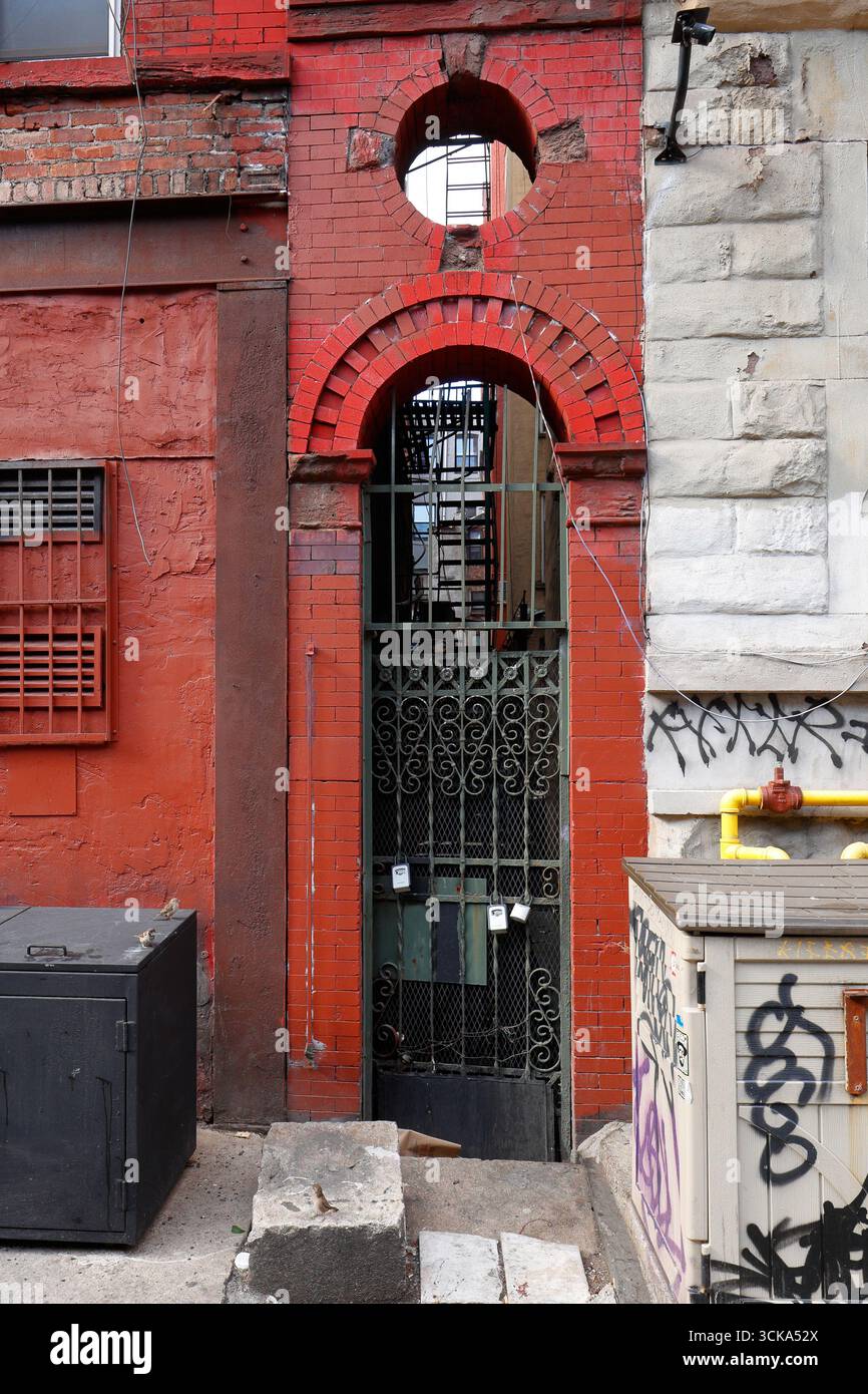 Un cancello metallico con arco in mattoni e portale rotondo che conduce in uno stretto vicolo tra due edifici. Foto Stock