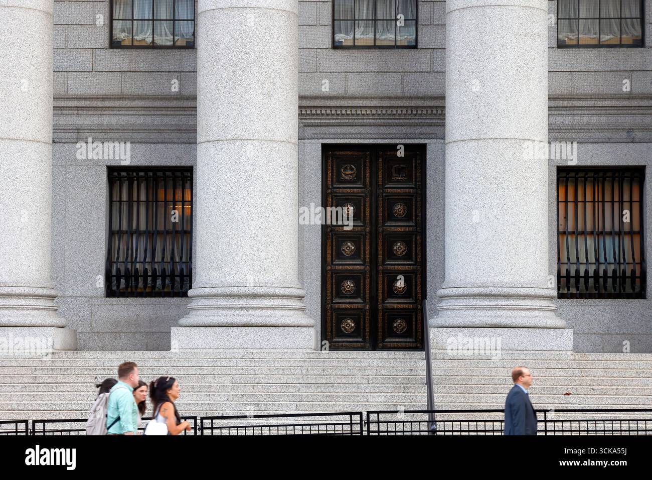La gente passa davanti a una porta di metallo ornata incorniciata tra due grandi colonne di pietra in un tribunale federale. Foto Stock