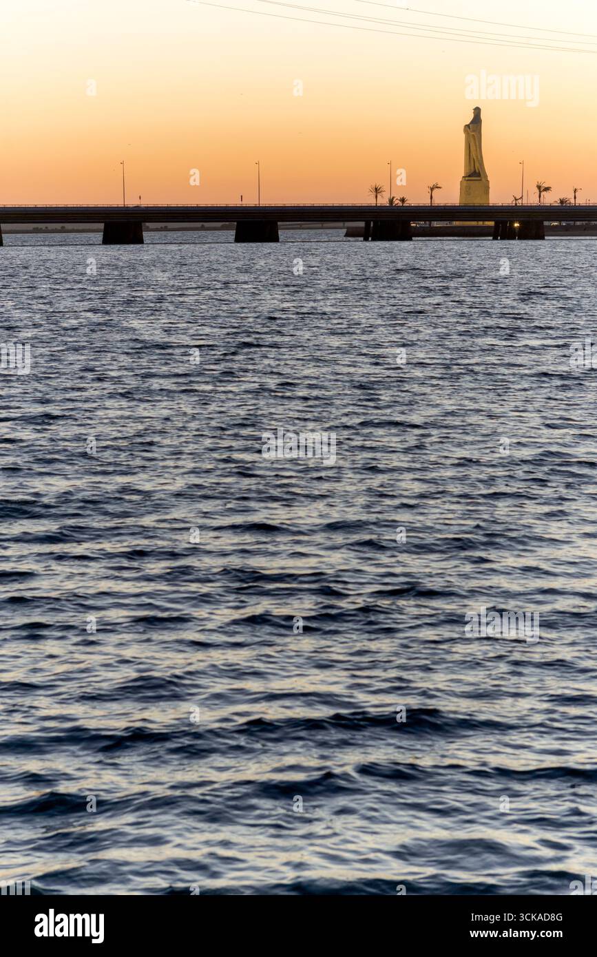 Monumento a la Fe Descubridora, Colón, agua del mar, puente de hormigón y colores cálidos del anochecer en Huelva, paisaje inspirador y simbólico. Foto Stock