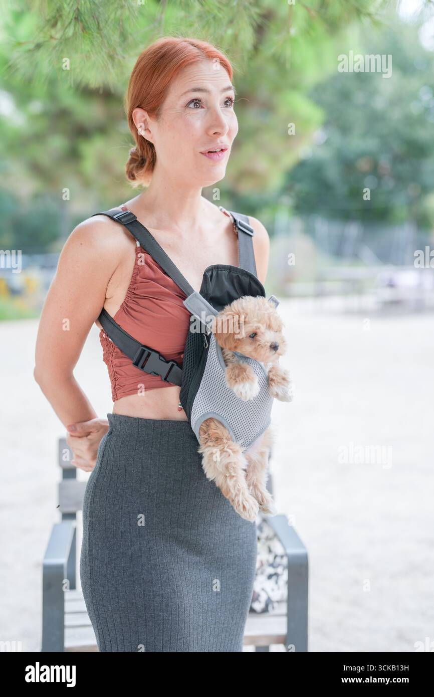 Una donna sta tenendo un cane piccolo in un portabagagli sulla schiena. Il cane indossa un maglione e si sta godendo il viaggio. La donna è in piedi accanto a un ben Foto Stock