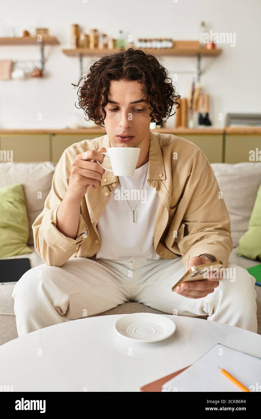 Un giovane e affascinante assapora il caffè mentre interagisci con il suo smartphone in un'atmosfera serena. Foto Stock