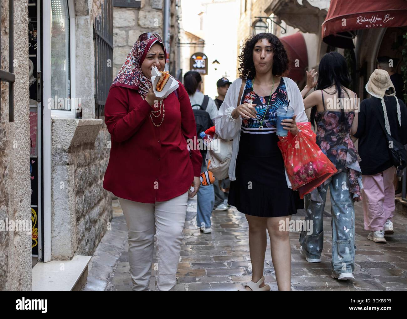 I turisti mangiano cibo di strada mentre camminano per le strette strade di pietra della città vecchia di Budva, in Montenegro. 8 settembre 2025. Foto Stock