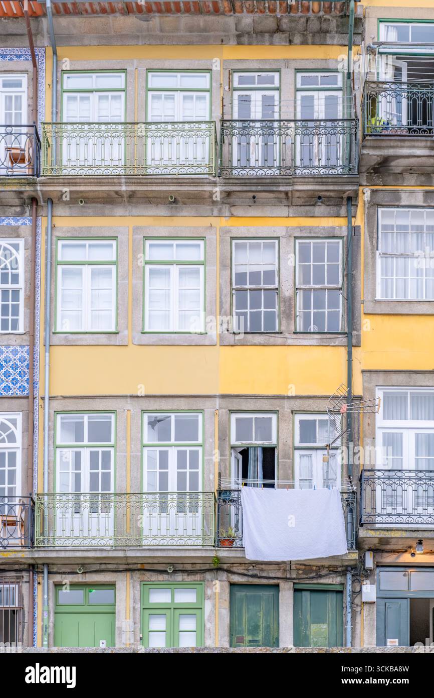 Facciata residenziale dai toni caldi con dettagli architettonici misti e balconi in ferro battuto a Porto, Portogallo. Pareti gialle e beige, mattoni a vista Foto Stock